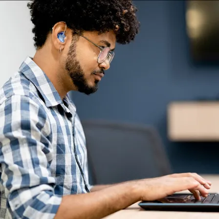 Un hemme assis avec aides auditives et main sur clavier d'ordinateur