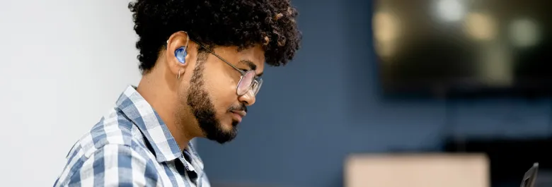 Un hemme assis avec aides auditives et main sur clavier d'ordinateur