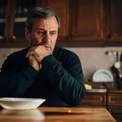 Photo d'un homme seul, le regard vide, devant une assiette vide